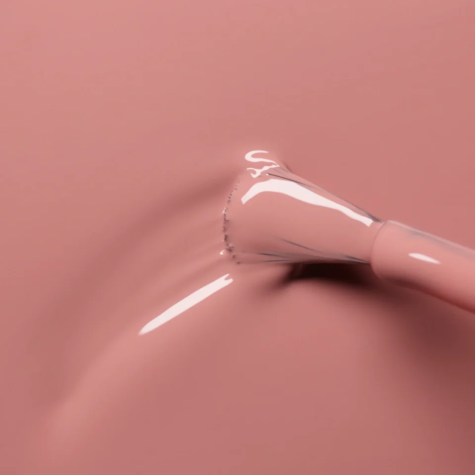 Tamsesnio rožinio atspalvio nagų lakas tepamas ant paviršiaus stambiu planu.